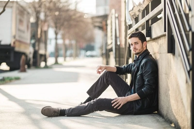 atlanta male actor wears leather jacket and sits on sidewalk of west midtown