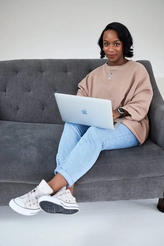 female entrepreneur works on laptop sitting on white wall woodstock couch