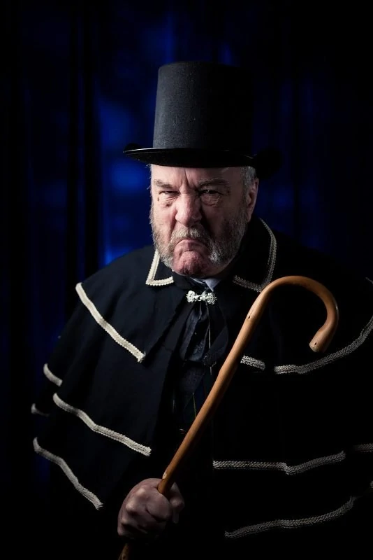 old man ebenezer scrooge looks grouchy with cane