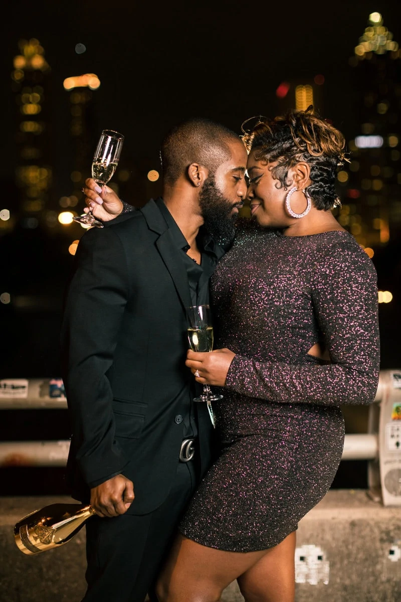 engaged couple shares glass of champagne over skyline at Jackson Street Bridge Atlanta