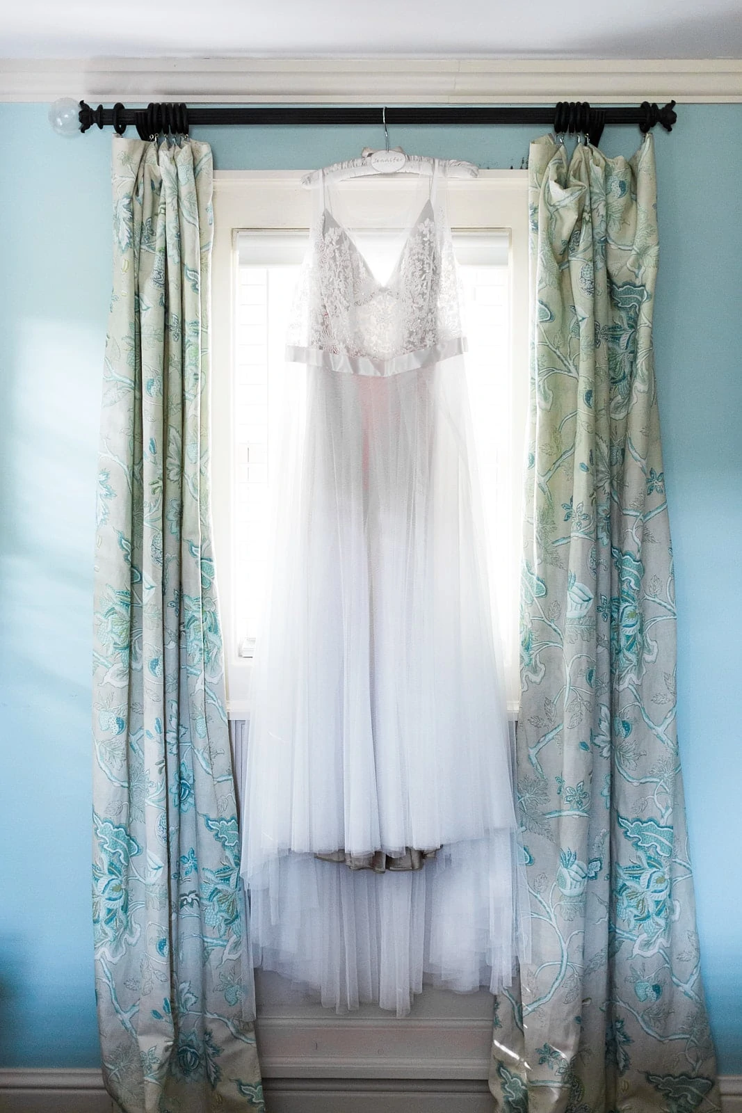 wedding dress hangs on window curtain Barnsley Gardens